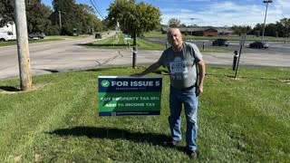 A supporter beside a For Issue 5 yard sign